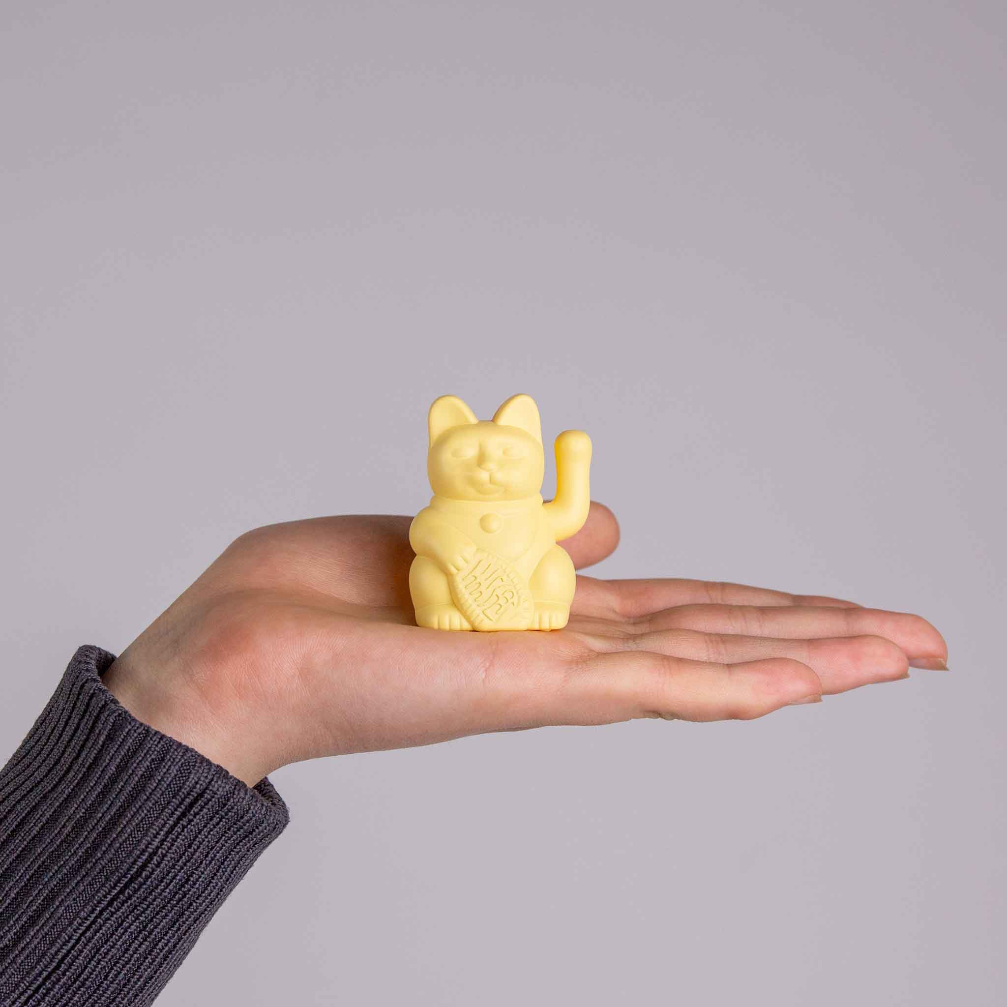 Eine gelbe Solar Winkekatze steht auf einer Hand als Größenvergleich