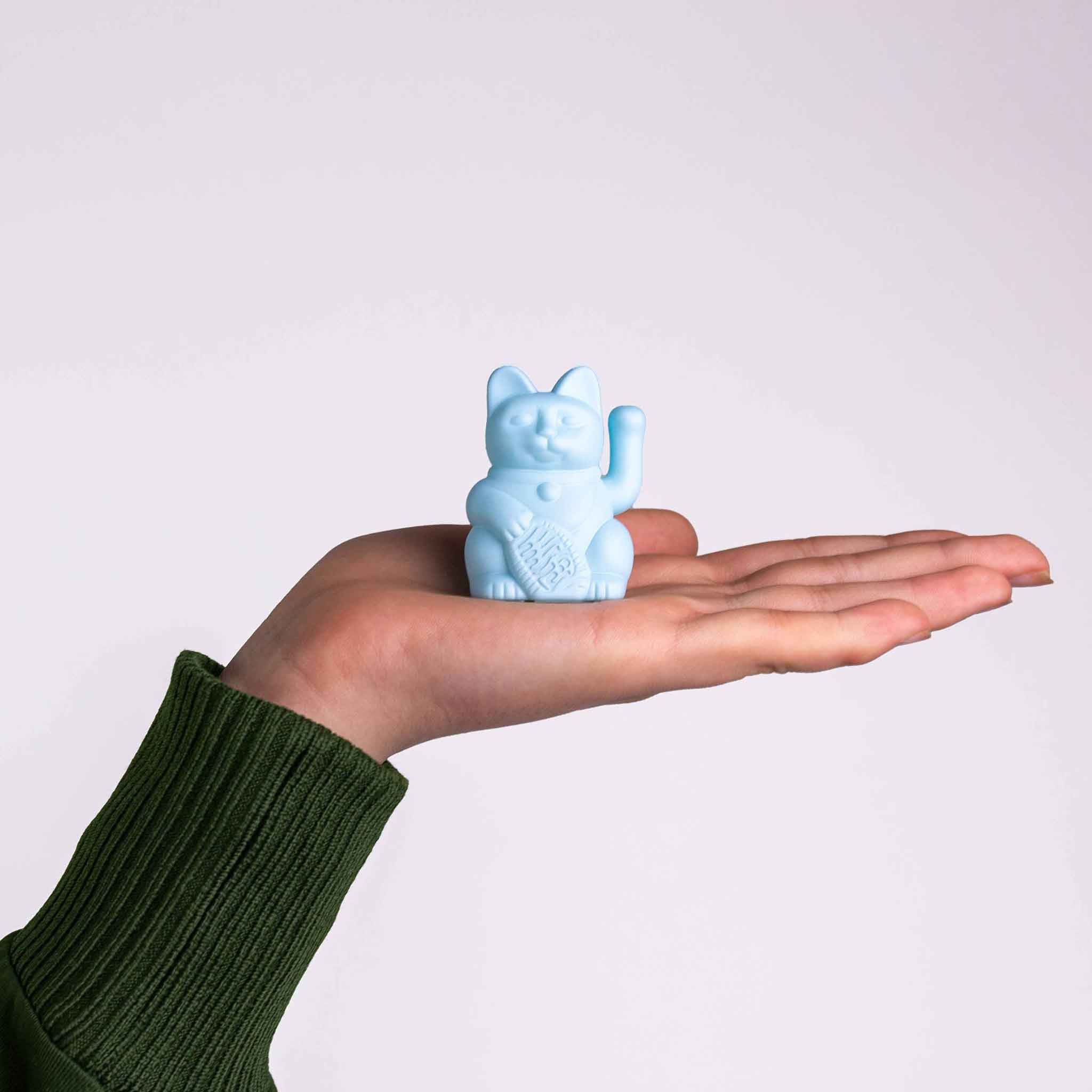 Eine Solr Winkekatze in Hellblau auf einer Hand als Größenvergleich